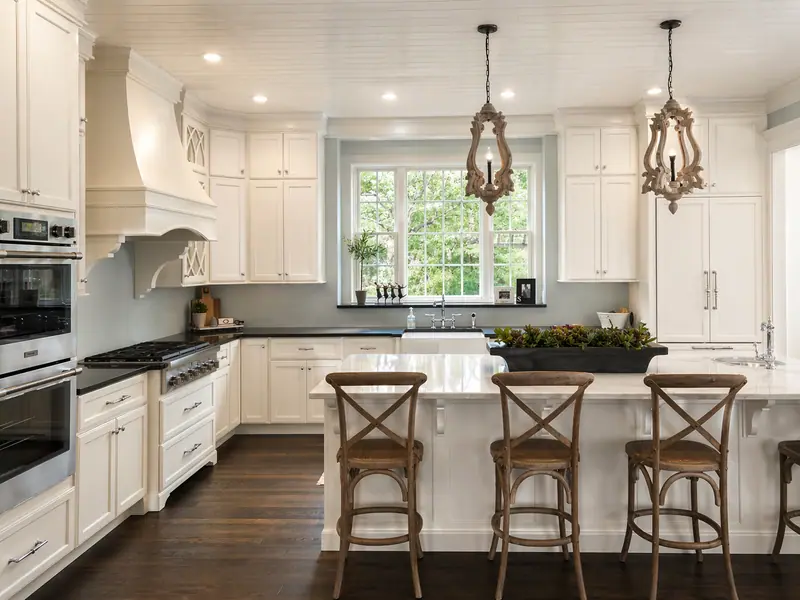 Cream kitchen with mullioned upper cabinets, carved wood chandeliers, and X-back counter stools